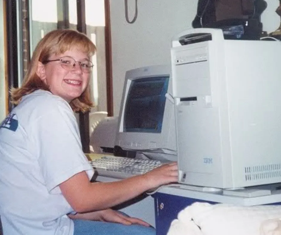 Randi as a child smiling beside a large desktop computer in 1997