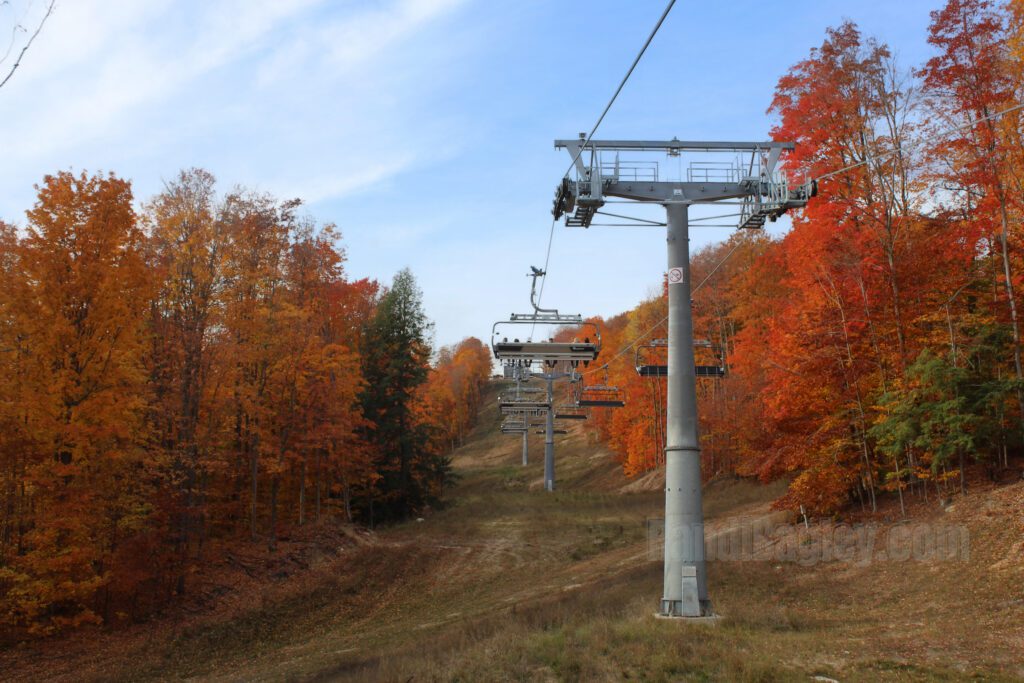 Boyne Mountain chairlift surrounded by vibrant fall foliage in shades of orange, red, and yellow.