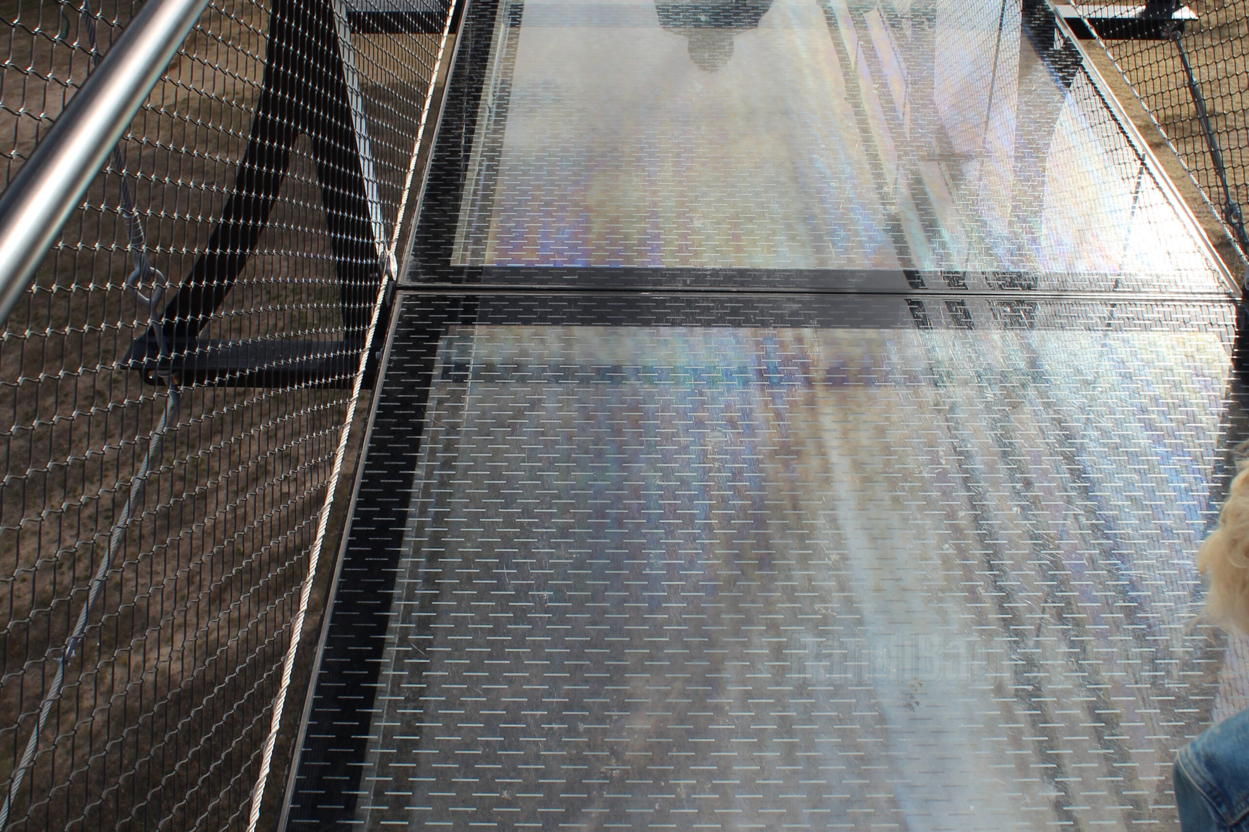 Glass floor section of SkyBridge Michigan with reflections and a view of the ground below.