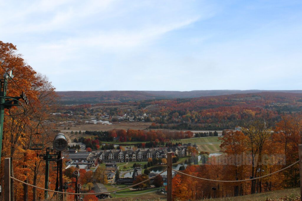 Panoramic view of Boyne Mountain Resort with colorful fall trees, buildings, and a pond below